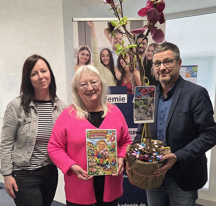 Auf dem Bild stehen drei Personen, links zwei Frauen und rechts ein Mann, mit einem Blumenstrauß in der Hand und lächeln in die Kamera.