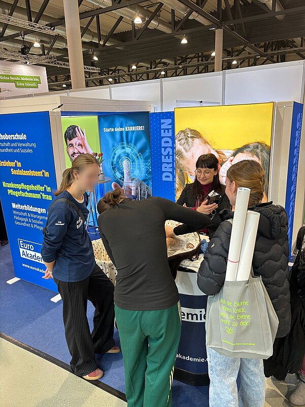 Drei junge Frauen am Messestand der Euro-Akademie üben an einer Puppe