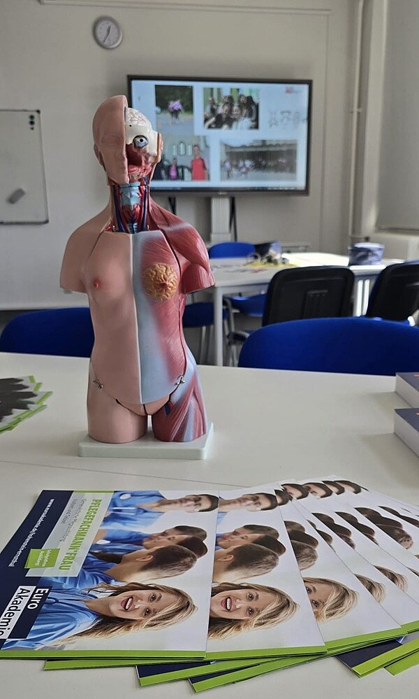 Auf einem Tisch steht ein Platiktorso mit hetausnehmbaren Organen, vor ihn liegen Informationskataloge der Euro Akademie.