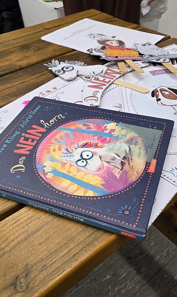 Kinderbuch „Das NEINhorn“ auf Holztisch; drumherum Bastelvorlagen und ausgeschnittene Figuren auf Stäbchen.
