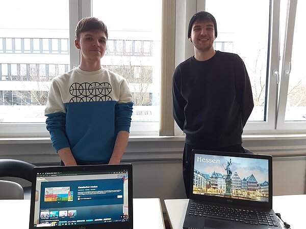 Der nächste Schritt zur Karriere: Career Week Zwei Schüler stehen vor einem Fenster im Klassenraum und zeigen auf den Laptops vor ihnen auf dem Tisch eine Präsentation mit dem Thema "Hessen".