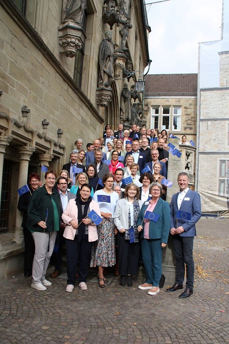 Die Schulleitungen der "Europaschulen in Niedersachsen" haben sich für ein Gruppenfoto auf der Treppe des Osnabrücker Rathauses aufgestellt. Sie halten alle kleine Europaflaggen aus Papier in der Hand.