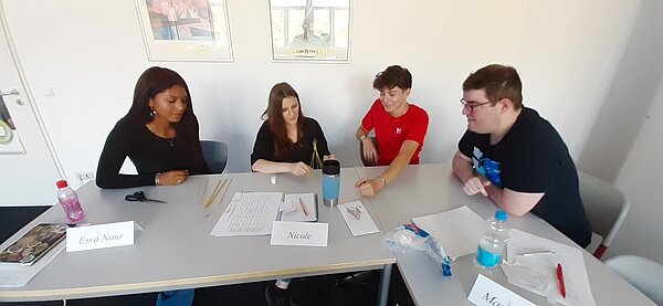 „Die Neuen“ sind da – Euro Akademie Mainz begrüßt neue Klasse der Fremdsprachenkorrespondenten Eine Gruppe von vier Personen sitzt an einem Tisch, baut mit Spaghetti und Marshmallows eine Konstruktion und lacht dabei.