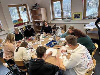Auszubildende sitzen gemeinsam an zusammengeschobenen Tischen und basteln Weihnachtsdekoration und Karten.