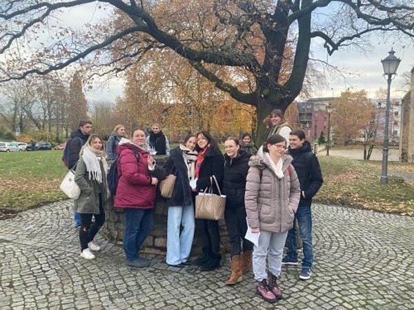 Eine Gruppe von Menschen steht lächelnd unter einem Baum in einem Park mit herbstlicher Kulisse.
