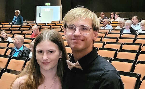 All That Jazz! Englischunterricht im Opernhaus Hannover Ein junges Paar steht im Theatersaal zwischen leeren Stuhlreihen und blickt in die Kamera. Beide wirken festlich gekleidet.