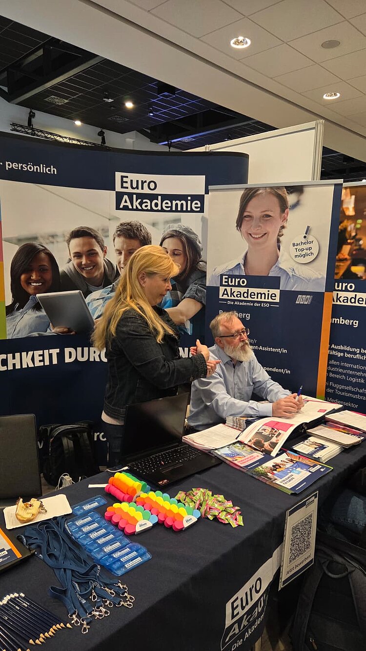 Zwei Mitarbeitende betreuen den Messestand der Euro Akademie und präsentieren Informationsmaterialien zu Ausbildungsangeboten.