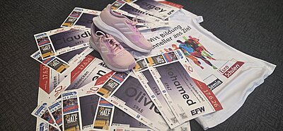 Laufunterlagen mit Startnummern, pinke Sportschuhe und ein Euro-Schulen-Laufshirt liegen auf dem Boden und bereiten auf eine Sportveranstaltung vor.