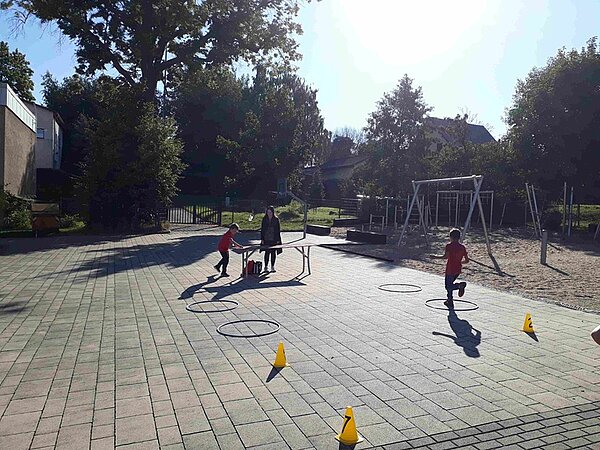 Kinder überqueren den Parcours mit Pylonen und Hula Hoop Reifen.