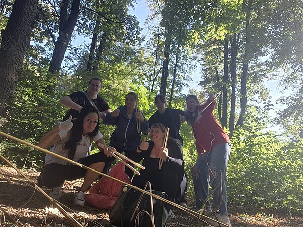Die Schülerinnen und Schüler der Euro Akademie Hohenstein-Ernstthal posieren im Wald für ein Gruppenfoto. Sie halten eine große rote Mülltüte und Müllzangen in den Händen und tragen teilweise Einmalhandschuhe.