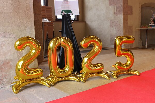 Ein Tag voller Glanz, Emotionen und unvergesslicher Erinnerungen Die Zahl 2025 in goldenen, großen Luftballons steht auf dem boden, neben dem ausgelegten roten Teppich.