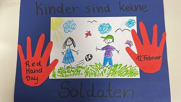 Ein Plakat zum Red Hand Day mit der Aufschrift ‚Kinder sind keine Soldaten‘ und ‚12. Februar‘. Im Zentrum befindet sich eine Kinderzeichnung mit zwei Kindern, die auf einer Wiese spielen. Um die Zeichnung herum sind rote Handabdrücke aus Papier geklebt.