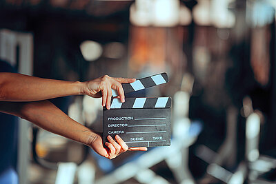 Eine Filmklappe wird vor einem unscharfen Hintergrund gehalten und symbolisiert den Start einer Video- oder Filmproduktion.