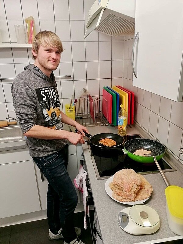 An die Töpfe, fertig, los! Auszubildender steht am Herd mit einer Pfanne in der Hand, in der er selbst ein Schnitzel zubereitet.