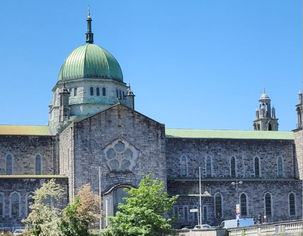 Die Kathedrale der irischen Küstenstadt Galway mit seiner bläulichen Kuppel in der Mitte ist zu sehen, davor ein paar grüne Bäume.