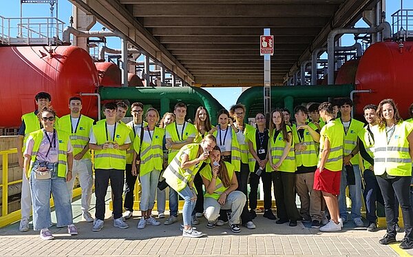 Fotografische Souvenirs vom Erasmus-Austausch in Barcelona Schülerinnen und Schüler posieren in neongelben Westen auf einem Fabrikgelände für ein Gruppenfoto.