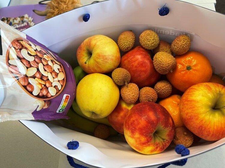 Eine mit Äpfeln, Clementinen, Litschis und einer Packung Nüsse gefüllte Tasche