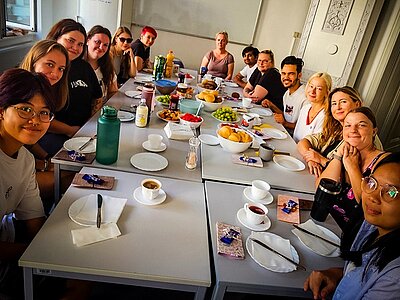 Die Auszubildenden im ersten Ausbildungsjahr sitzen mit ihrer Lehrerin um einen großen Tisch beim gemeinsamen Frühstück.