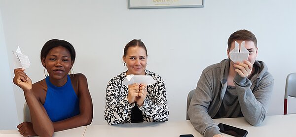 „Die Neuen“ sind da – Euro Akademie Mainz begrüßt neue Klasse der Fremdsprachenkorrespondenten Drei Personen sitzen nebeneinander und halten ihre selbst gebastelten Origami-Tiere und Figuren in die Kamera, einer verdeckt halb sein Gesicht damit.