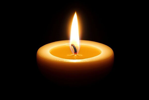 Eine einzelne, helle Kerze sitzt in der Mitte eines schwarzen Hintergrundes, deren warme gelbe Flamme einen sanften Schein auslöst.