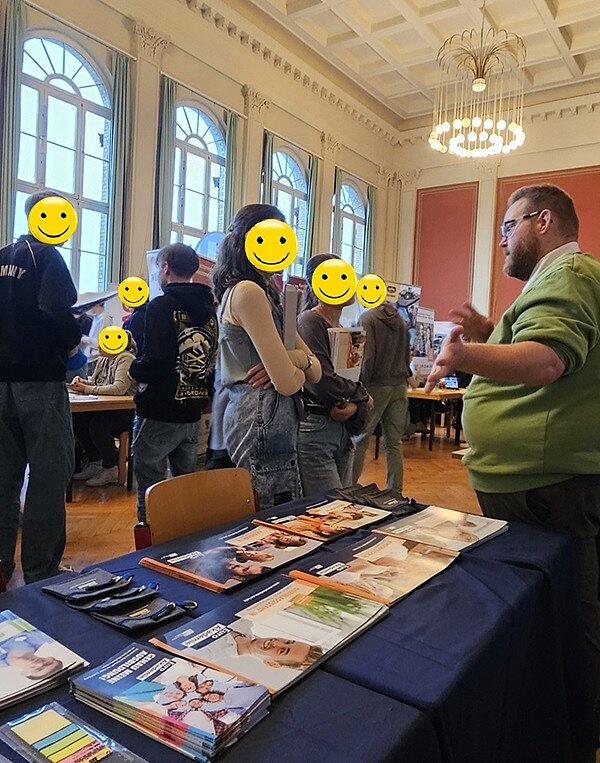 Mitarbeiter am Messestand der Euro Akademie im Beratungsgespräch mit zwei interessierten Schülerinnen.