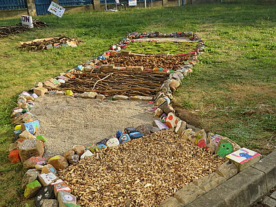 Auf einer Wiese ist aus verschiedenen Materialien ein Barfußpfad gelegt, gesäumt von bunt bemalten Steinen.