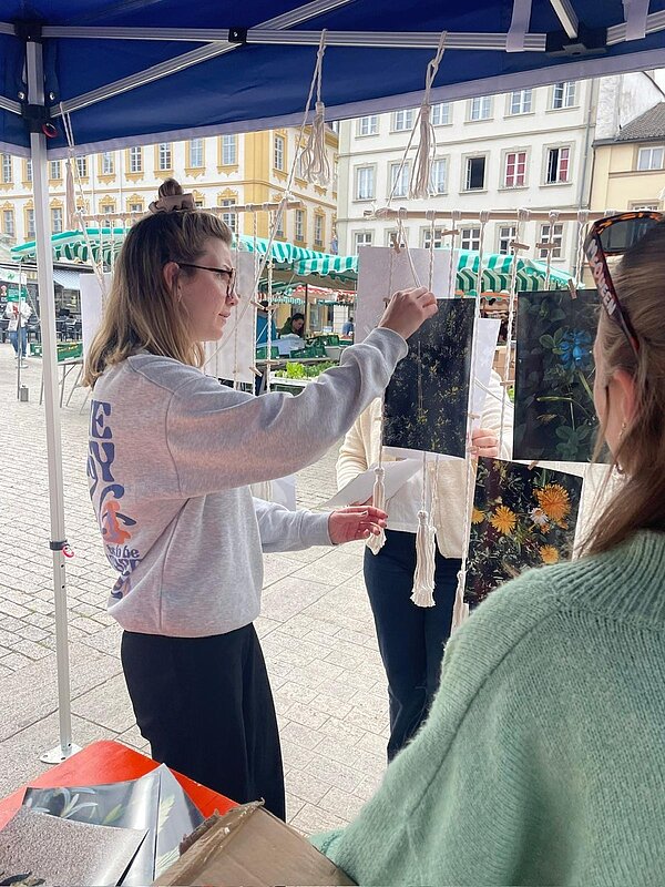 Unter einem Pavillon befestigen Personen Fotos und Kunstwerke mit Klammern an einer dekorativen Schnurinstallation.
