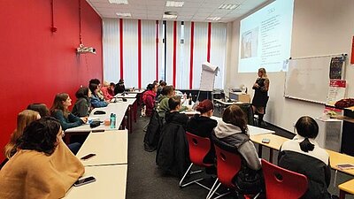 Schüler sitzen in zwei langen Reihen hintereinander im Klassenzimmer und hören dem Vortrag aufmerksam zu. 