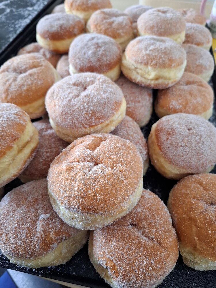 Mehrere mit Zucker bestreute Berliner beziehungsweise Pfannkuchen liegen zum Teil gestapelt auf einem Backblech.