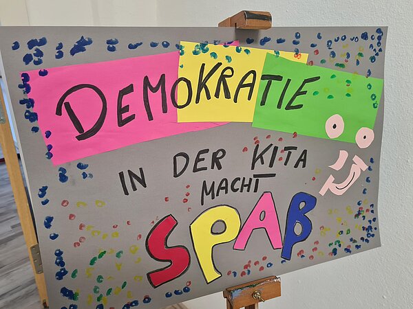 Ein bunter Plakat mit der Schrift Demokratie in der Kita.