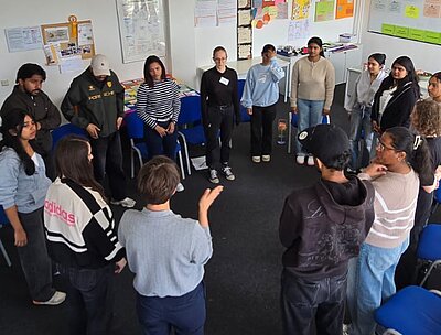 Teilnehmende stehen in einem Klassenraum im Kreis und diskutieren gemeinsam während eines Workshops.