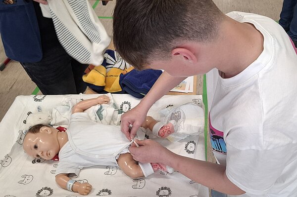Ein Schüler übt an einer Babypuppe das Wickeln und Anziehen im Rahmen einer praxisnahen Ausbildungssituation.