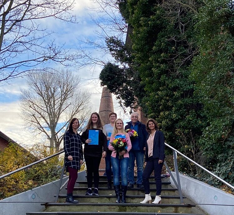 Feierliche Verabschiedung Die Absolventen posieren mit ihren Zertifikaten und Blumen in der Hand auf Treppenstufen für ein Gruppenfoto.