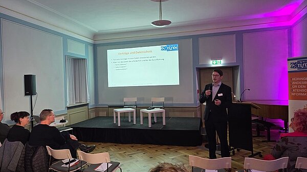 Schülerinnen und Schüler sitzen in einem großen Raum und schauen nach vorn zum Referenten und der Präsentation zum Thema Datenschutz.