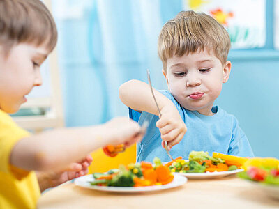Das Bild zeigt zwei Jungs, die gesundes Gemüse essen. Es betont die Bedeutung einer ausgewogenen Ernährung im jungen Alter.