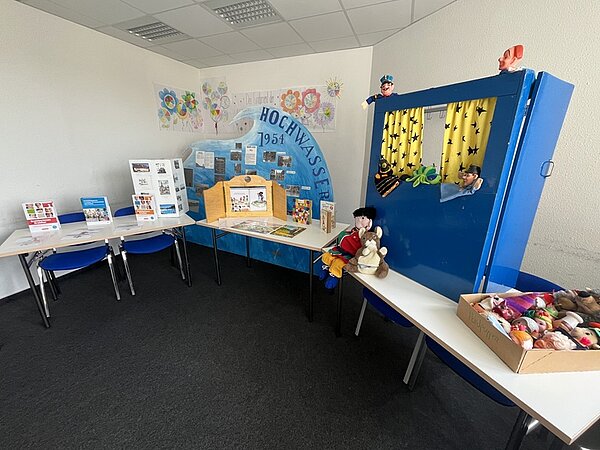 Tag der offenen Tür In einem Klassenraum sind die Tische an die Wand geschoben, ein großes blaues Puppentheater steht darauf, unterschiedliche andere Unterrichtsmterialien und Informationen zum Hochwasser sind ausgestellt.