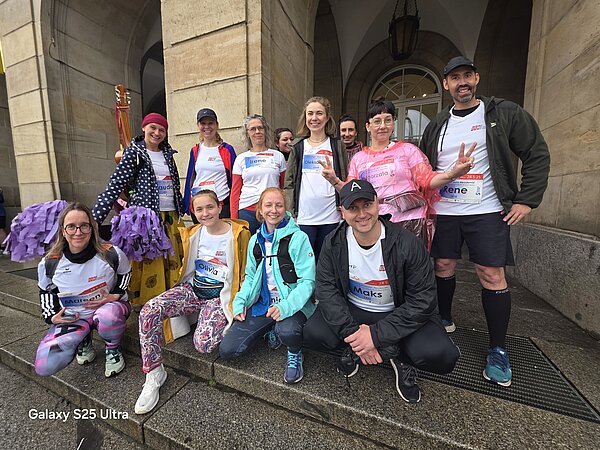 Gruppenfoto vor einem McDonald's-Bogen mit zwölf Teilnehmenden der REWE Team Challenge, darunter viele mit Startnummern und Namensschildern.