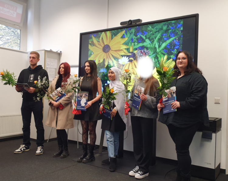 Die Absolventinnen und Absolventen erhielten zum Abschluss Blumen und posieren für ein Gruppenfoto.