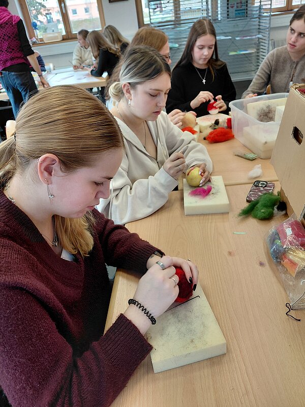 Mehrere Schülerinnen bearbeiten farbige Wollkugeln auf Schaumstoffplatten und filzen konzentriert weihnachtliche Figuren.