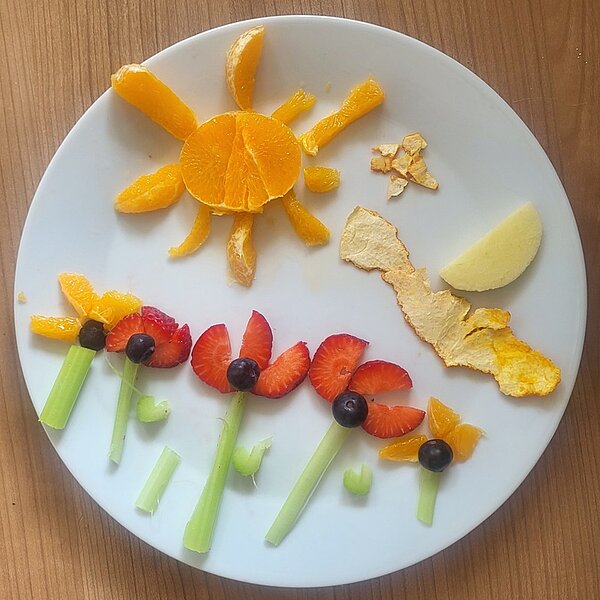 Eine Mandarine als Sonne und eine Blumenwiese mit Tulpen aus Erdbeeren auf dem Teller. 
