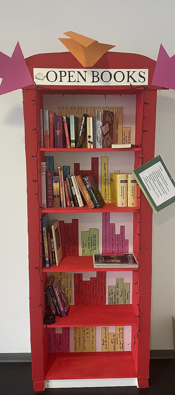 „Open Books“- Nachhaltiger Umgang mit Literatur Ein aus Papier und Pappe selbstgebasteltes Bücherregal mit einem Schild "Open Books", in dem einige Bücher stehen.