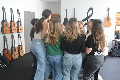 Mädchen und junge Frauen tanzen in einem großen weißen Raum, an dessen Wände Noten in Schwarz angemalt sind.