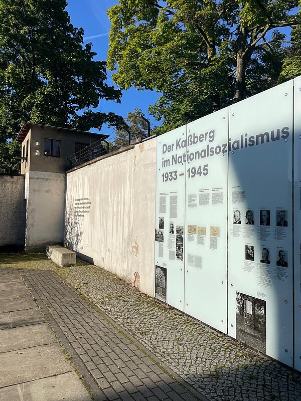 Außenansicht des Kaßberg-Gefängnisses mit Infotafel zur Geschichte im Nationalsozialismus (1933–1945). Links ein Wachturm, rechts große Glasplatten mit Texten und Fotos als Gedenkinstallation.