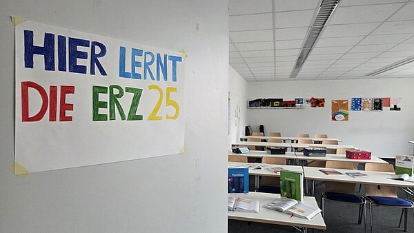 Ein Klassenzimmer angehender Erzieherinnen und Erzieher der Euro Akademie Erfurt zeigt ein Whiteboard, Computer und farbenfrohe Poster an den Wänden. An der Tür hängt ein selbst gestaltetes Bild, auf dem steht "Hier lernt die ERZ 25".