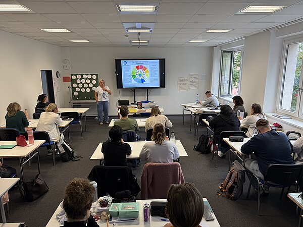 Foto einer Schulklasse, die einer Referentin bei einem Vortrag lauscht
