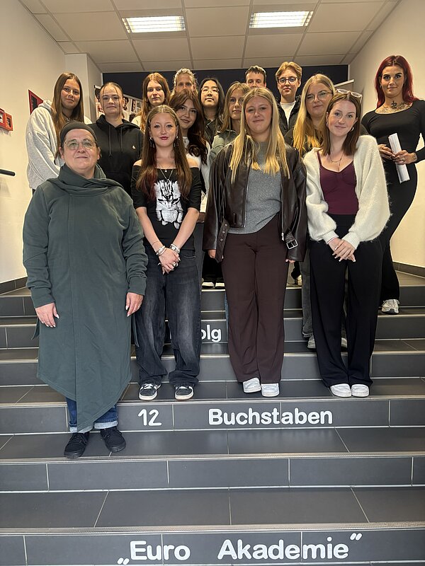 Gruppe von Schülerinnen, Schülern und Mitarbeitenden der Euro Akademie Zwickau posiert im Schulgebäude gemeinsam auf einer Treppe für ein Erinnerungsfoto.