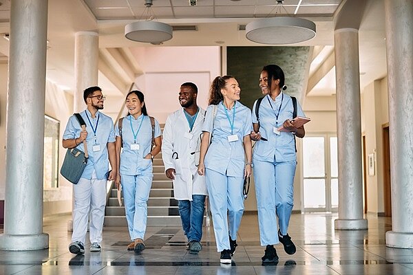 Rekordzahl an Auszubildenden in der Pflegefachausbildung Eine multi-ethnische Gruppe lächelnder Pflegeauszubildender unterhält sich auf einem Flur.