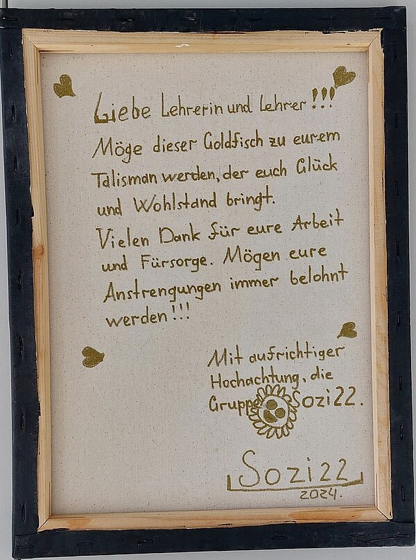 Feierliche Übergabe der Zeugnisse Auf der Rückseite eines Bilderrahmens stellt folgender Text: Liebe Lehrerin und Lehrer!!! Möge dieser Goldfisch zu eurem Talisman werden, der euch Glück und Wohlstand bringt. Vielen Dank für eure Arbeit und Fürsorge. Mögen eure Anstrengungen immer belohnt werden!!! Mit aufrichtige Hochachtung, die Gruppe Sozi22. Sozi22, 2024. Der Text ist in Gold geschrieben und mit goldenen Herzen in den Ecken verziert.