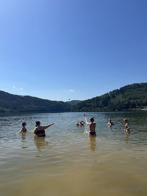 Eine Gruppe junger Menschen steht in einem See und spielt mit einem Ball.