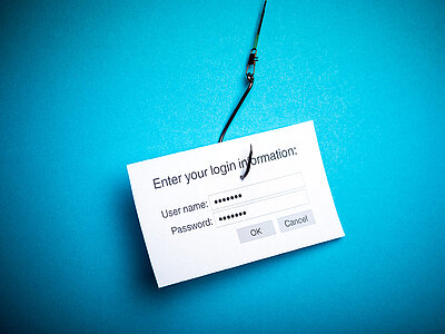 Ein weißes Blatt Papier mit einem Login-Formular ist an einem Angelhaken befestigt. Das Formular enthält Felder für Benutzername und Passwort sowie die Schaltflächen 'OK' und 'Abbrechen'. Der Hintergrund ist blau.
